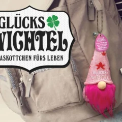 Rosa Glückswichtel am Rucksack befestigt, dazu das Logo mit dem Schriftzug ‚Glückswichtel – Maskottchen fürs Leben‘