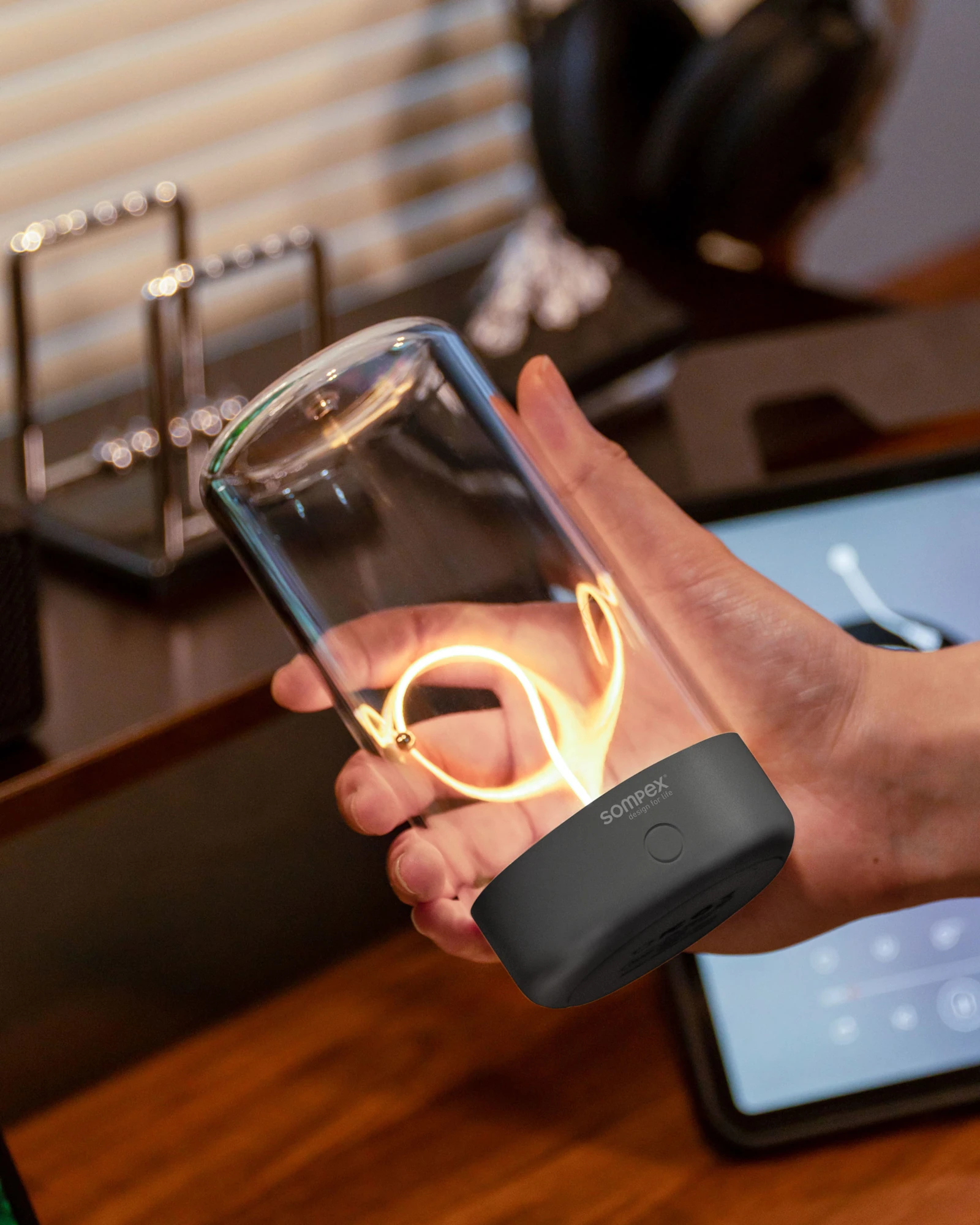 Eine Hand hält die Akku-Tischleuchte PULSE by Sompex über einem Schreibtisch